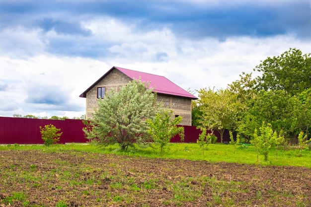 Twostory country house behind a fence and a plot with a garden Village life