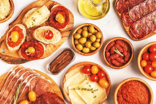 Typical spanish tapas concept. Concept include slices jamon, chorizo, sausage, bowls with olives, tomatoes, anchovies,  mashed chickpeas, cheese.