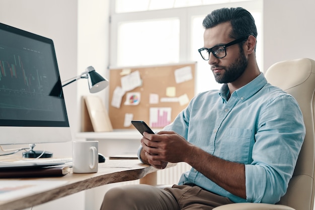 Typing business message. Young modern businessman using smart phone while sitting in the office