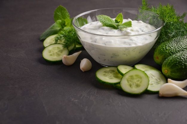 Tzatziki sauce and ingredients. Fresh cucumber and dill sauce on dark background.