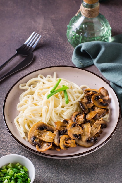 Udon noodles fried champignons and greens on a plate on the table vertical view