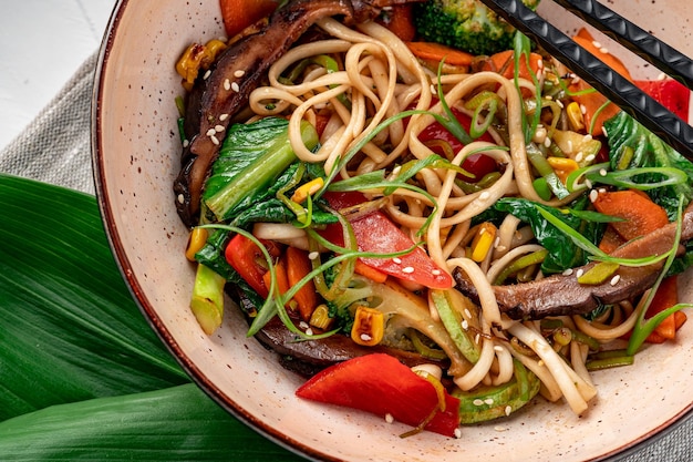 Udon stir fry noodles with beef meat and vegetables in a plate on white wooden background