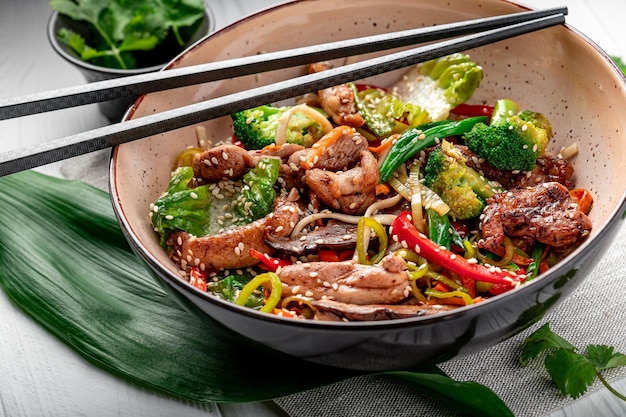 Udon stir fry noodles with pork meat and vegetables in a plate on white wooden background