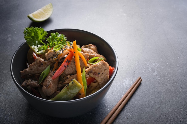 Udon stirfry noodles with pork bowl and chopsticks on black stone background asian cuisine