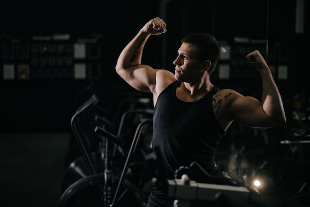 UFA, RUSSIA - 31 OCTOBER 2019. Muscular strong man with perfect beautiful body wearing sportswear standing in pose Champion in dark modern gym. Concept of healthy lifestyle.