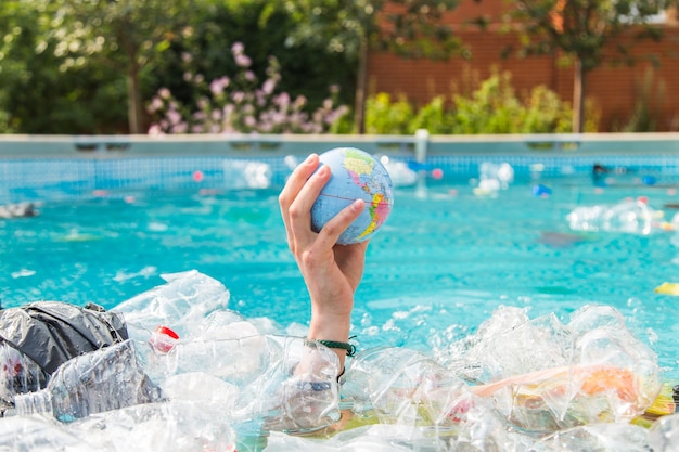 UFA, RUSSIA - JULY 25, 2019 : Problem of trash, plastic recycling, pollution and environmental concept - Plastic rubbish pollution in water environment, Earth globe is floating in the trash.