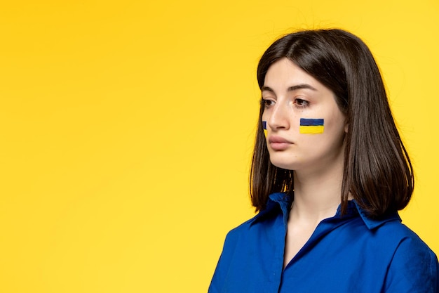 Ukraine russian conflict young pretty girl flags on cheeks yellow background close up upset