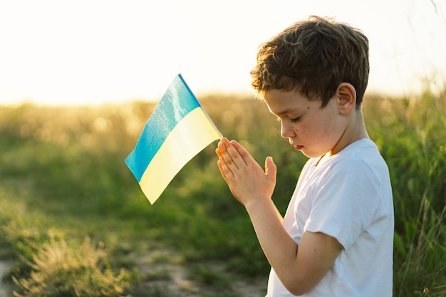 Ukrainian boy closed her eyes and praying to stop the war in Ukraine in a field at sunset Hands folded in prayer concept for faith spirituality and religion War of Russia against Ukraine Stop War