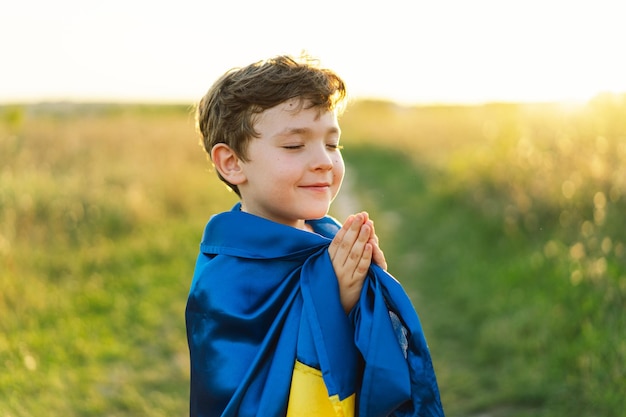 Ukrainian boy closed her eyes and praying to stop the war in Ukraine in a field at sunset Hands folded in prayer concept for faith spirituality and religion War of Russia against Ukraine Stop War