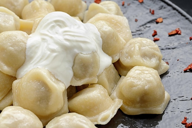 Ukrainian dumplings with sour cream on a black glossy plate Close up