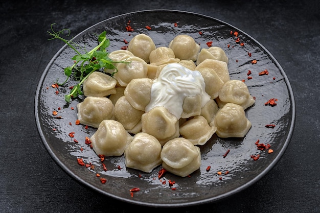 Ukrainian dumplings with sour cream and microgreen on a black glossy plate on a dark background