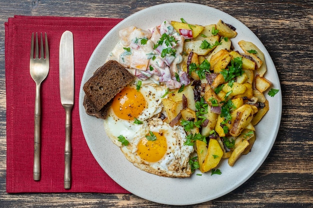 Ukrainian food fried potatoes with onions eggs vegetable salad black bread on wooden background