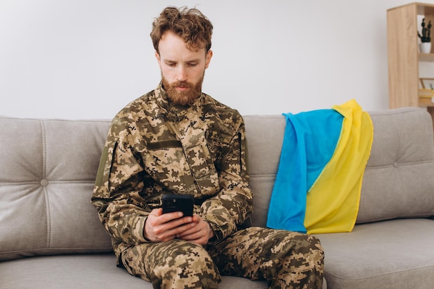 A Ukrainian soldier in military uniform is sitting on a sofa in the office and talking on the phone