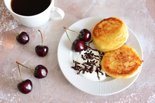 ukrainian syrniki on white plate with cherries and chocolate