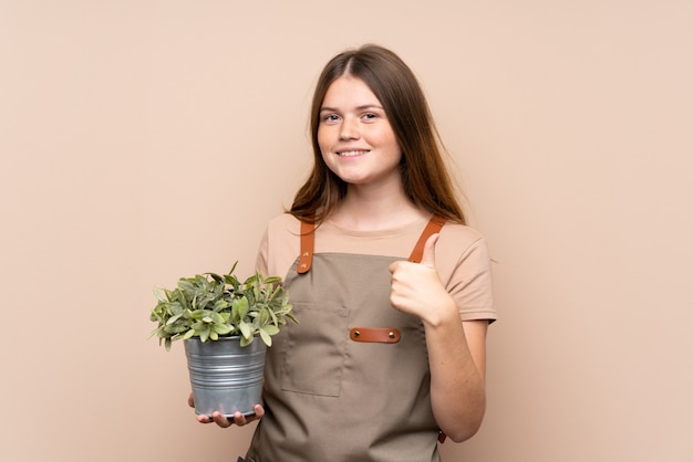 Ukrainian teenager gardener girl holding a plant giving a thumbs up gesture