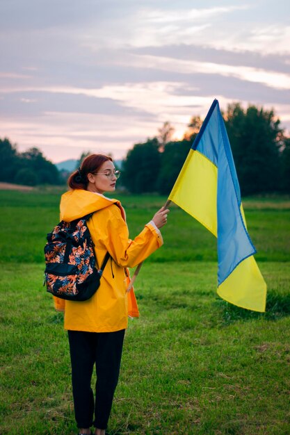 Ukrainian woman in the field with a large flag of Ukraine Patriotic photos Beautiful woman in a yellow raincoat