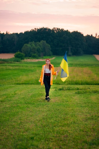 Ukrainian woman in the field with a large flag of Ukraine Patriotic photos Beautiful woman in a yellow raincoat