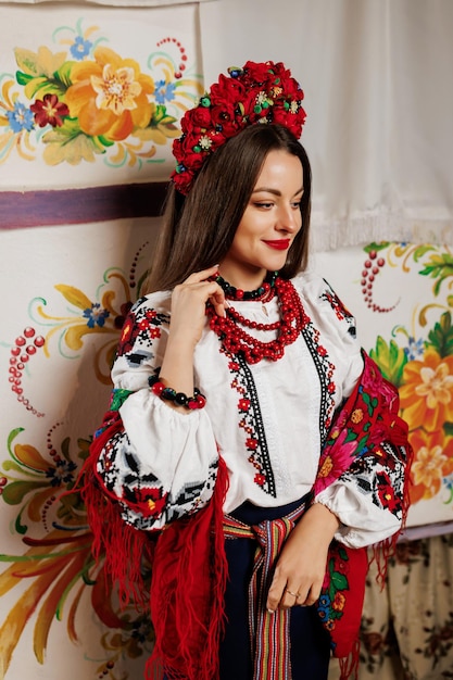 Ukrainian woman in traditional ethnic clothing and floral red wreath on background of decorated stove in hut Ukrainian national embroidered dress call vyshyvanka Pray for Ukraine