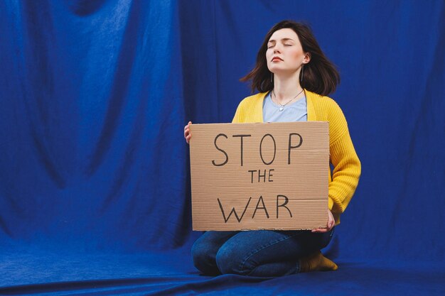 A Ukrainian woman in a yellow sweater and blue jeans with a stop the war sign Ukrainian girl suffered from the war No war