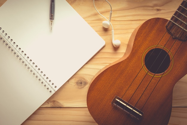 Ukulele guitar with earphone on wooden table , vintage