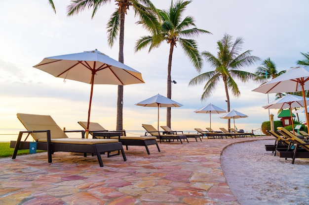 Umbrella and chair around swimming pool in hotel resort with sunrise in morning - holiday and vacation concept