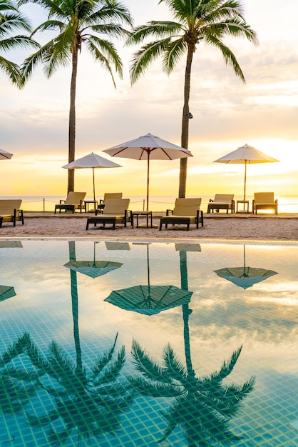 Umbrella and chair around swimming pool in hotel resort with sunrise in morning holiday and vacation concept