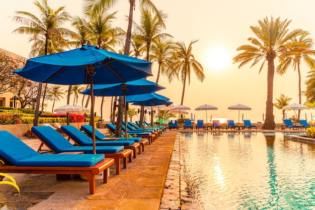 umbrella and chair at pool with palm trees at sunrise