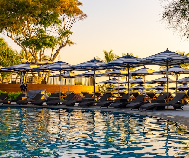 Umbrella and pool bed around outdoor swimming pool in hotel resort for travel holiday vacation