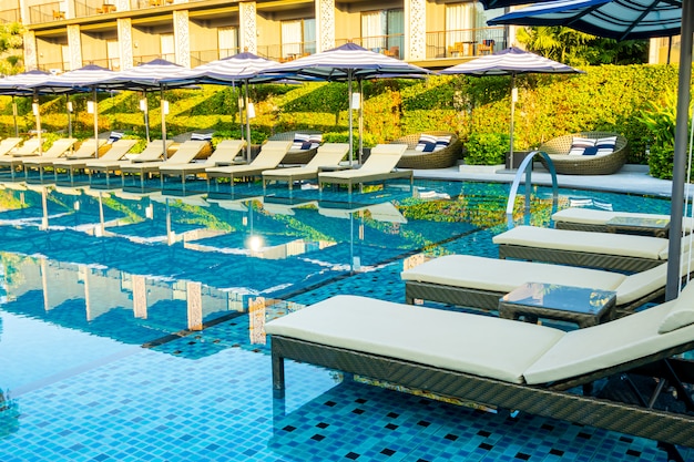 Umbrella and pool bed around outdoor swimming pool in hotel resort for travel holiday vacation