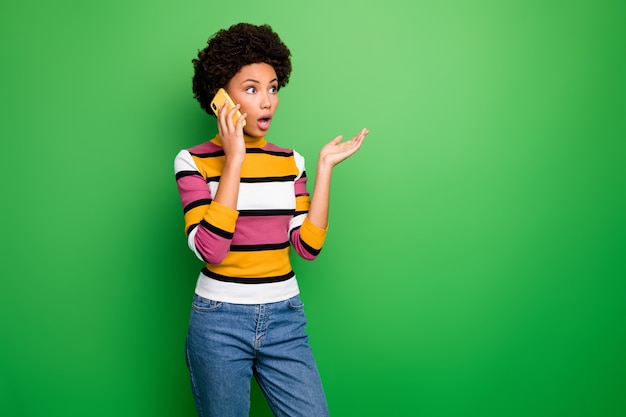 Unbelievable!  of pretty shocked dark skin wavy lady holding telephone speaking best friend listen awful bad news wear casual striped jumper jeans 