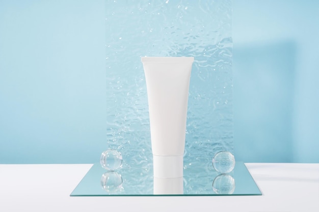 Unbranded cosmetic cream white plastic tube mockup on blue background with stylish props mirror and glass balls acrylic plate Body and health care beauty product packaging