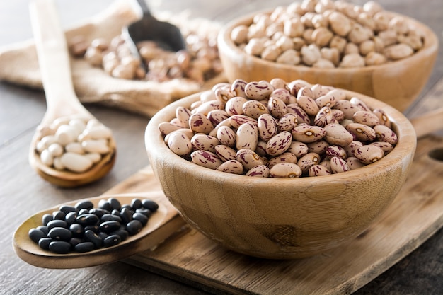 Uncooked assorted legumes in wooden bowl on wooden table