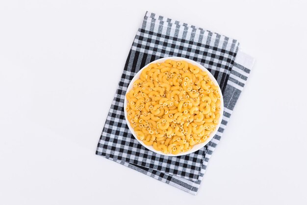 Uncooked chifferi rigati pasta in white cup on black checkered towel