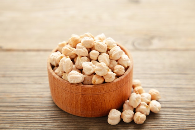 Uncooked dried chickpeas in wooden bowl on wooden