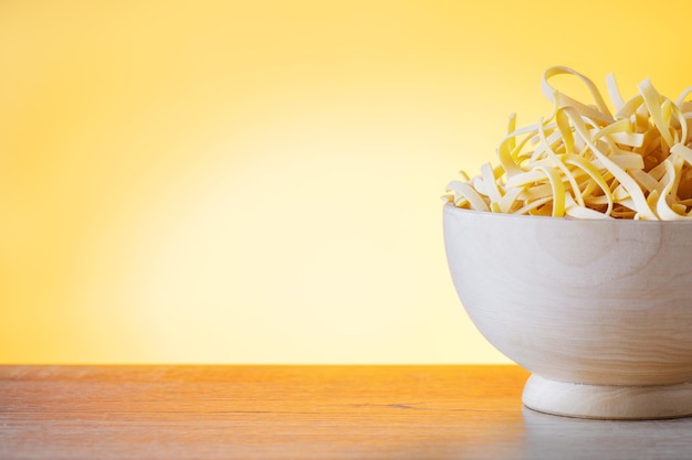 Uncooked dry pasta in wooden bowl on golden background with copy space