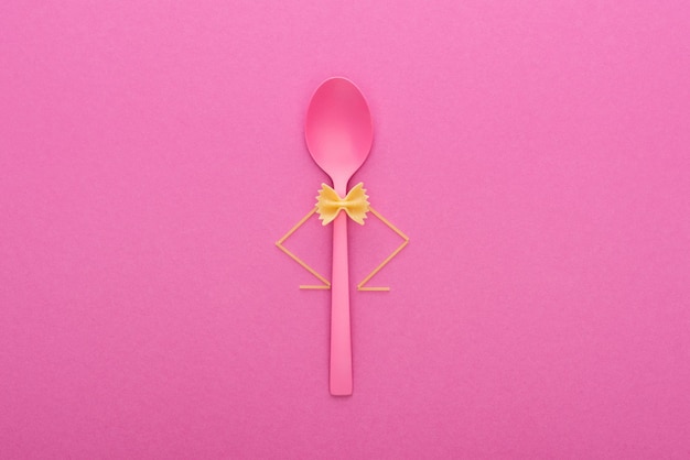 uncooked farfalle pasta on plastic spoon and spaghetti isolated on pink