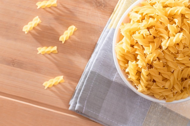 Uncooked fusilli pasta in white bowl on wooden board