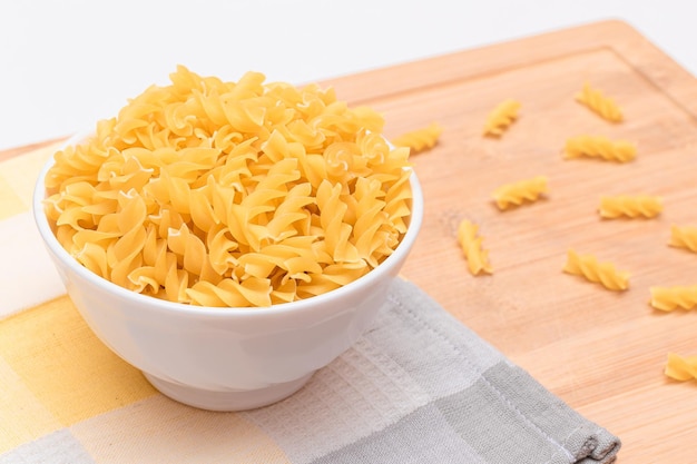 Uncooked fusilli pasta in white bowl on wooden board