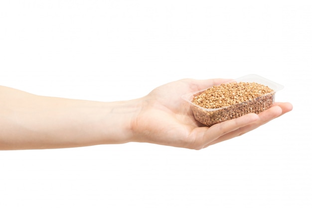 Uncooked heap brown buckwheat in transparent plastic container in men's hand 