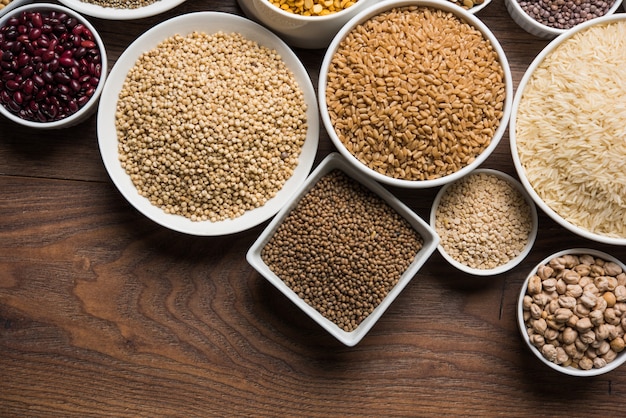 Uncooked Indian pulses,grains and seeds in White bowls over wooden surface. selective focus