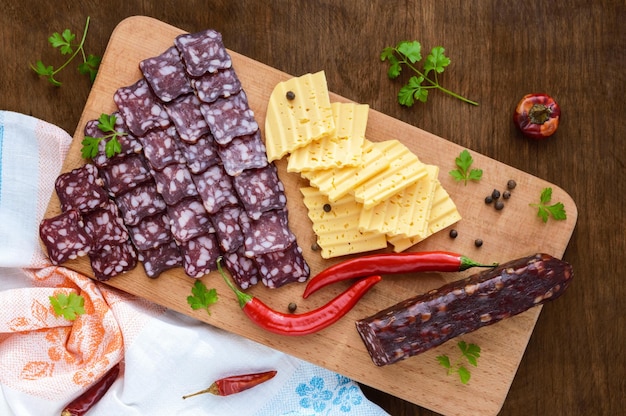 Uncooked jerked sausage cheese cutting slices on a cutting board on a dark wooden background