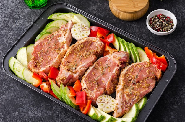 Uncooked pork steak with bell peppers and zucchini on a baking tray for roasting