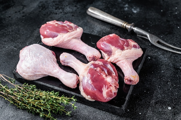 Uncooked Raw Duck legs drumsticks on marble board. Black background. Top view.