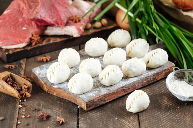 Uncooked raw homemade dumplings with meat beef and onion jusai on a board with flour on a dark wood.