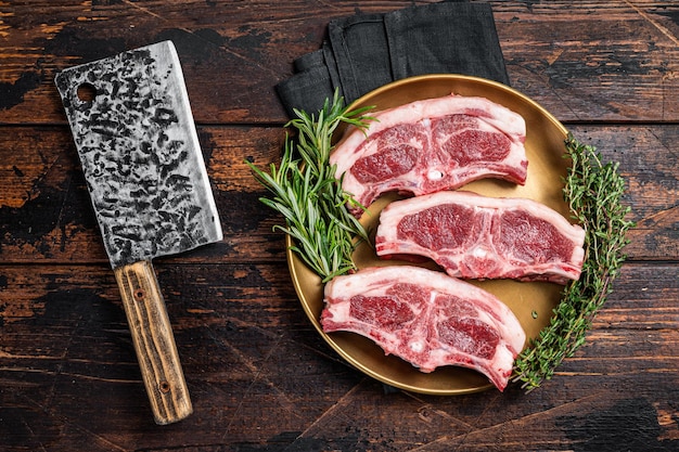 Uncooked Raw lamb loin chops steaks saddle in plate with rosemary and thyme Wooden background Top view