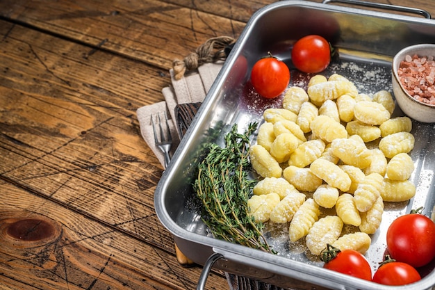 Uncooked Raw potato gnocchi in kitchen steel tray with herbs Wooden background Top view Copy space