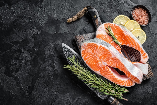 Uncooked Raw Salmon Fish Steaks on butcher board with herbs Black background Top view Copy space