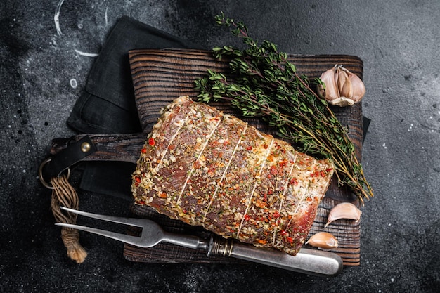 Uncooked spicy pork meat roulade prepared to roast with herbs and spices Black background Top view