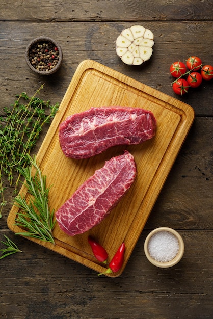 Uncooked two top blade beef steak on wood board with spices and herbs