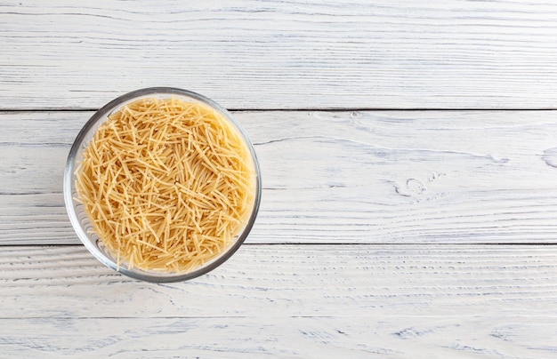 Uncooked vermicelli pasta in glass bowl on white wooden table